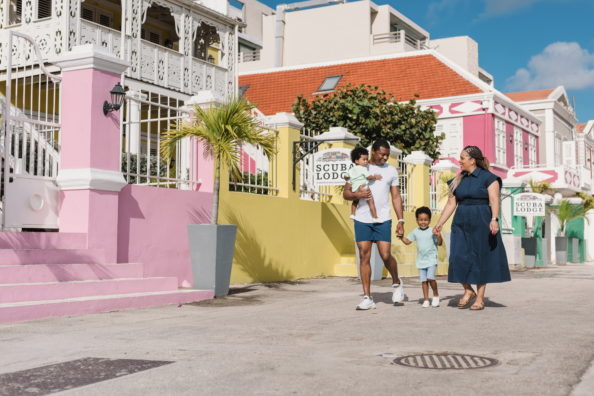 Family of four walking past pastel buildings and the Scuba Lodge sign in Pietermaai