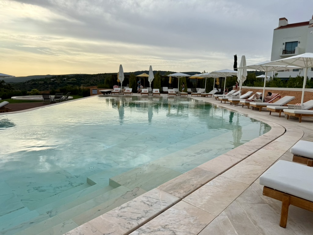 Resort pool at sunset with loungers, umbrellas and hills in the distance
