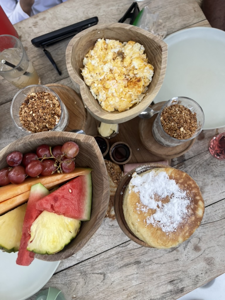Breakfast spread of scrambled eggs, granola parfaits, fresh fruit and pancakes on a weathered wood table