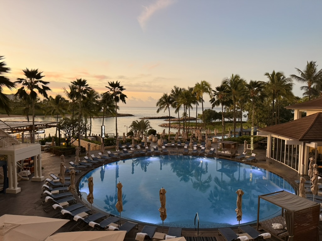 The same resort pool at sunset, lit blue against a golden sky