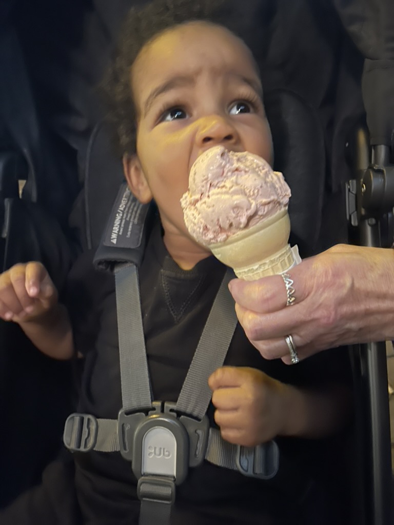 Toddler in a stroller taking a bite of a strawberry ice cream cone