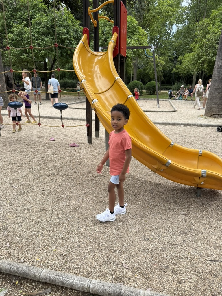 Boy standing beside a yellow slide at a shaded playground in María Luisa Park