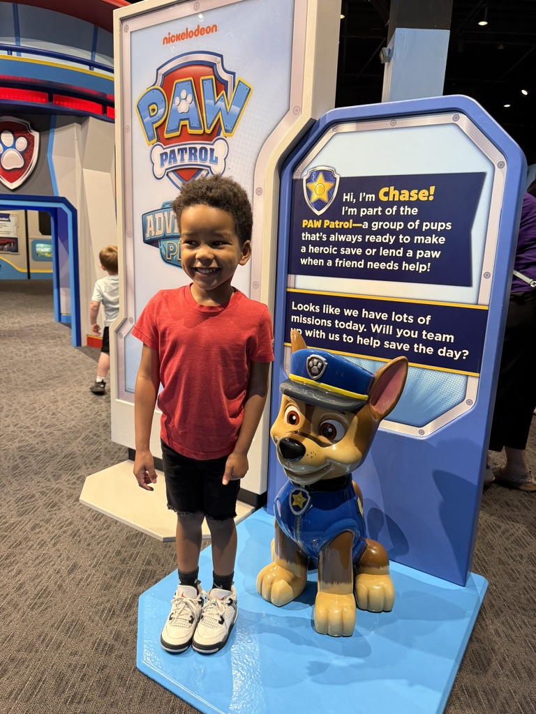 Preston standing beside a life-size Chase statue at the PAW Patrol Adventure Play entrance