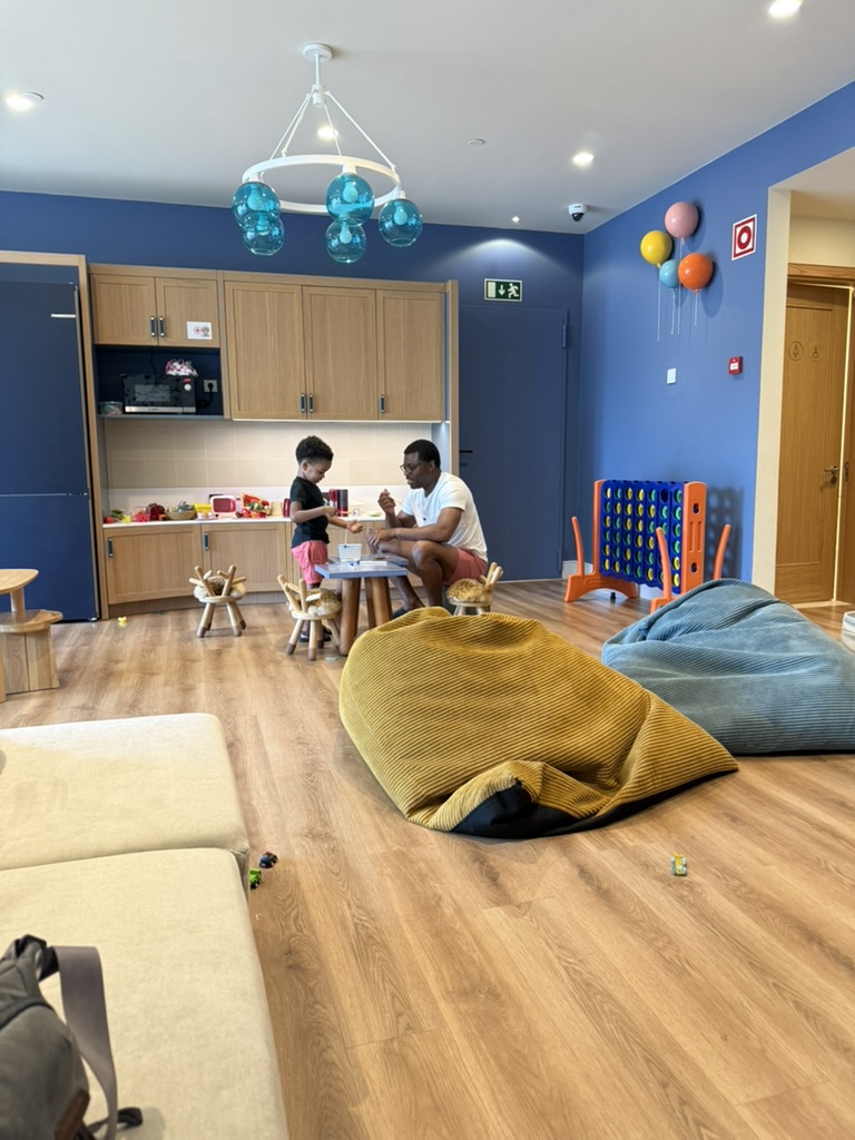Blue-walled kids' club room with a play kitchen, bean bags and a giant Connect Four game