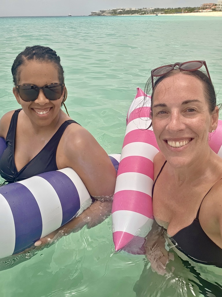 Two friends smiling on striped water hammocks in clear turquoise water