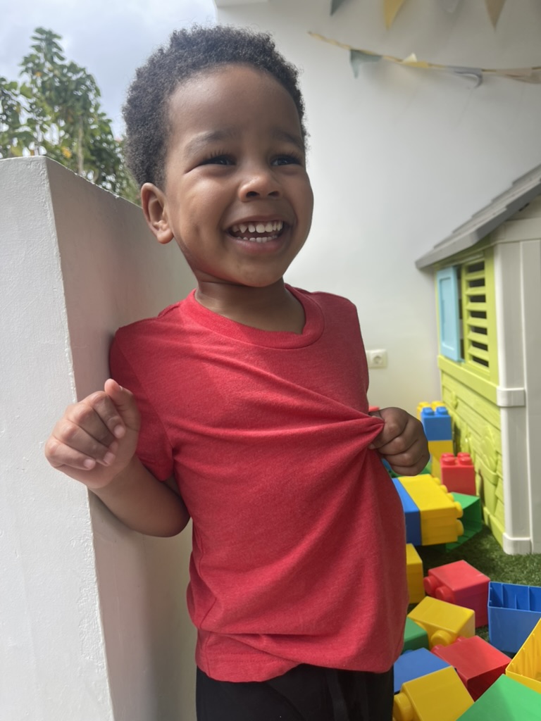 Laughing toddler in a red shirt beside the villa's outdoor playhouse and foam blocks