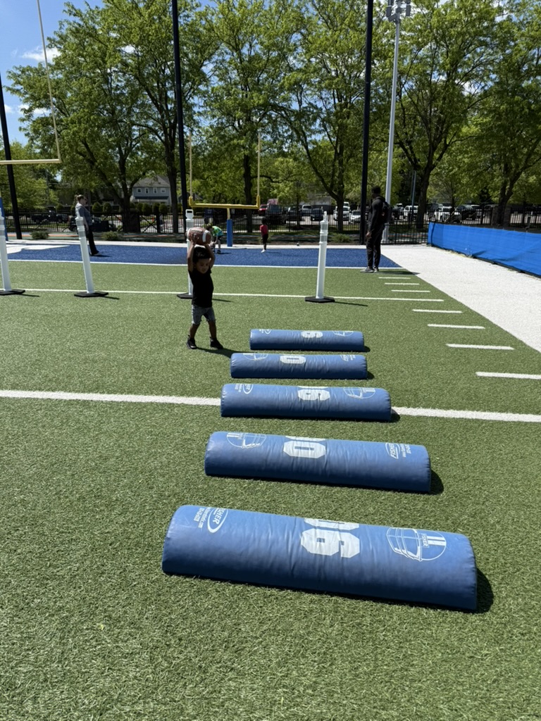 Avery lifting a football overhead beside blocking dummies on the museum's outdoor turf field