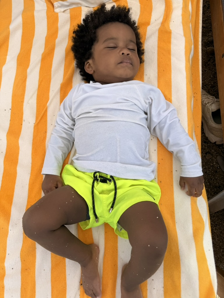 Toddler asleep on an orange and white striped beach towel on a lounger