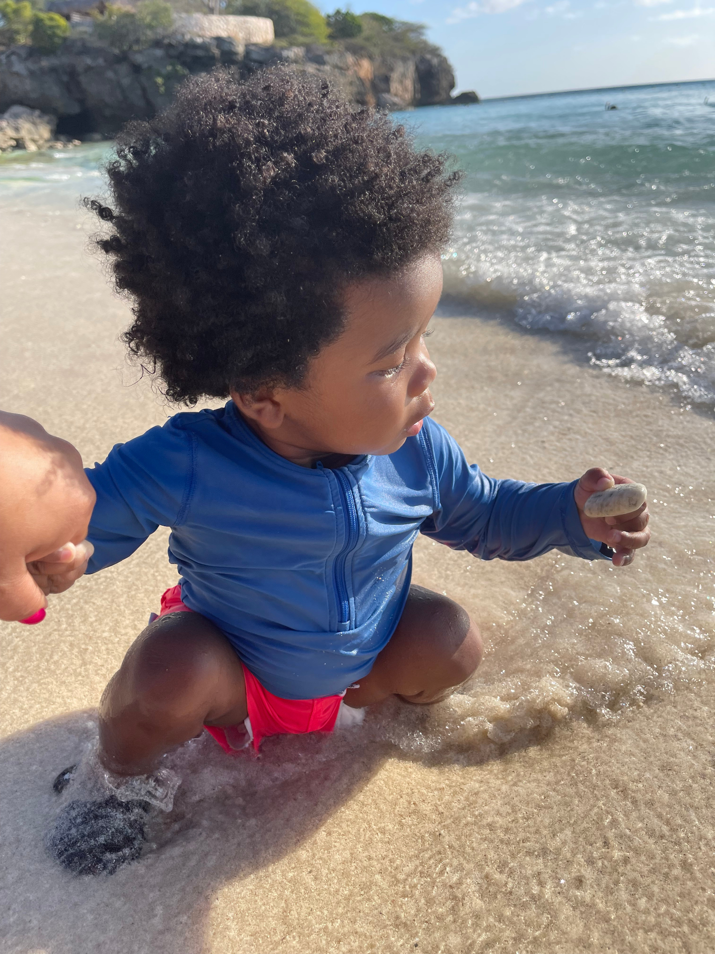 A toddler crouching at the shoreline holding a stone at Grote Knip