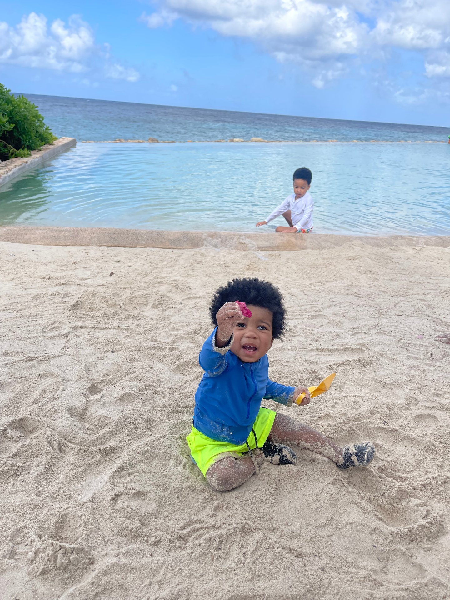Two young boys playing in the sand beside a protected swimming area in Curaçao