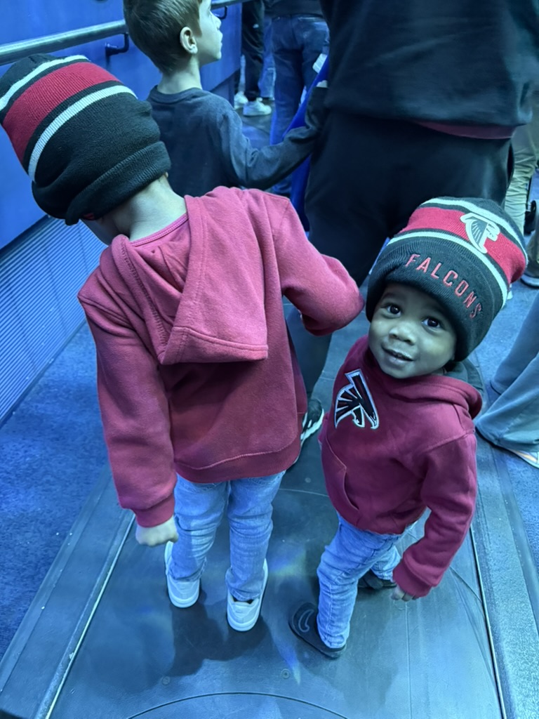 Preston in a Falcons beanie looking up while walking the aquarium walkway with his brother